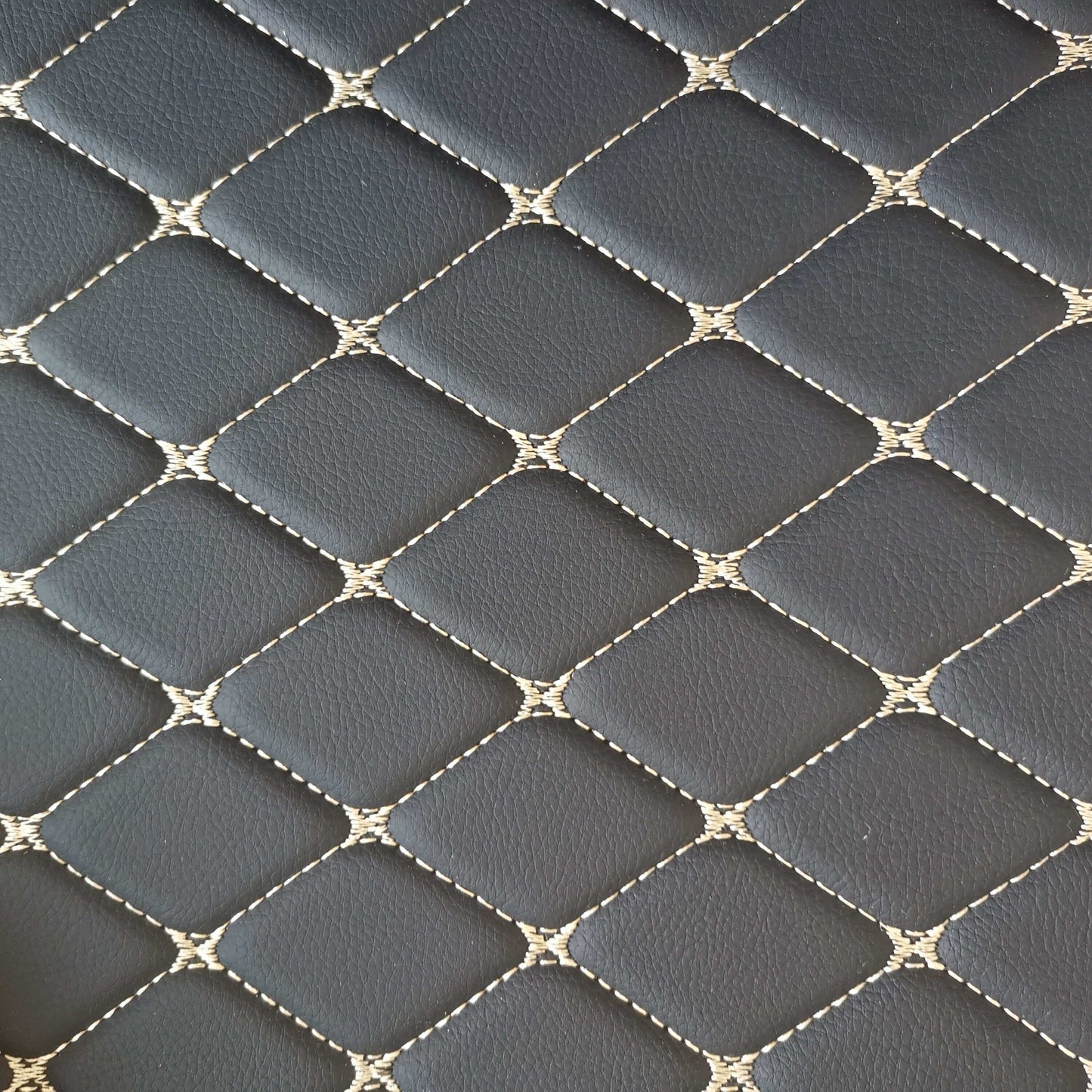 Close-up of diamond-stitched black car mat material with beige stitching for luxury car interiors.
